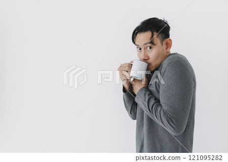 Cold man in grey fleece base layer drinking hot drink isolate on white. 121095282