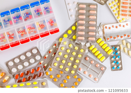 Different types of tablets, capsules are arranged along with weekly pill organizer on clean surface. 121095633