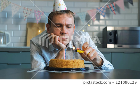 On a quiet birthday, a lonely man gazes at his cake, lighted candles flickering, embracing a bittersweet moment 121096129