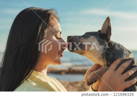 young woman in profile holding sheepdog puppy who licks her on nose 121096320