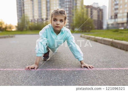 serious girl 7 years old primary school student in sports clothes took stand at starting position on street on road outdoor 121096321
