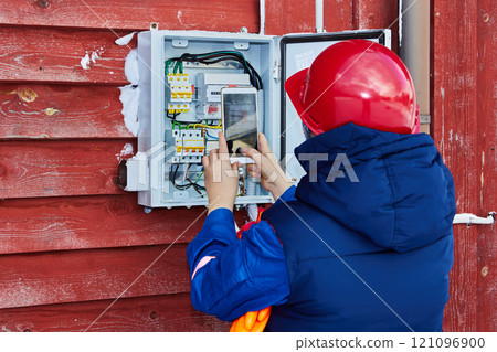 Electrical engineer takes readings of external electric meter in private house to submit electricity meter reading to energy company. 121096900