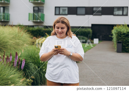 Smiling woman text messaging on smart phone at sunny day. Urban lifestyle concept. Happy woman chatting on phone and relaxing outdoors. 121097114