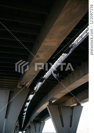 view from below of arches of suspension road. bridge over water, expressway against sky. 121097156