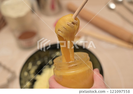 Christmas homemade baking, ingredients for baking gingerbread, woman with honey dipper added honey from the jar to the dough 121097558