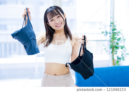 A young woman choosing clothes and underwear in the living room, choosing a sports bra and underwear A young woman choosing clothes and underwear in the living room, choosing a sports bra and underwear 121098153