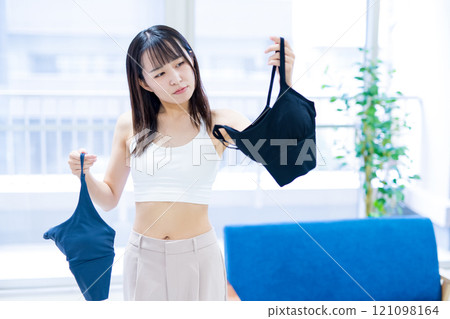 A young woman choosing clothes and underwear in the living room, choosing a sports bra and underwear 121098164