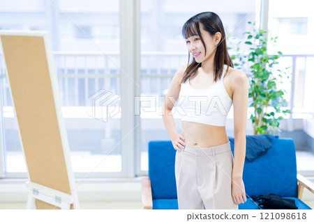 A young woman choosing clothes and underwear in front of a full-length mirror, choosing a sports bra and underwear 121098618