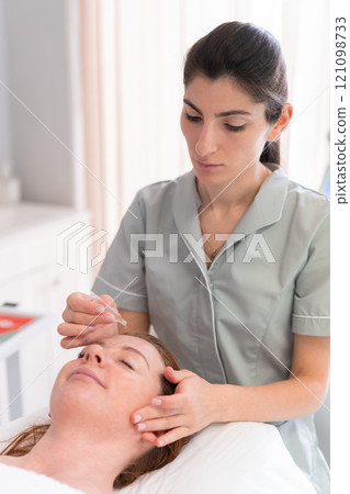 Female cosmetologist dripping serum drops on woman Female cosmetologist dripping serum drops on woman 121098733