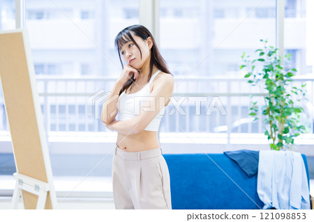 一位年輕女士在穿衣鏡前選擇運動胸罩和內衣時感到困惑。 121098853