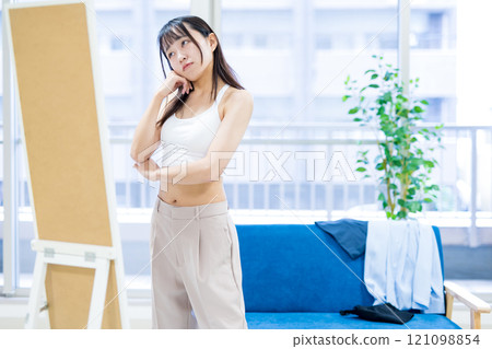 一位年輕女士在穿衣鏡前選擇運動胸罩和內衣時感到困惑。 121098854