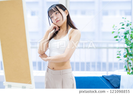 一位年輕女子在穿衣鏡前挑選運動胸罩和內衣時感到困惑。 121098855