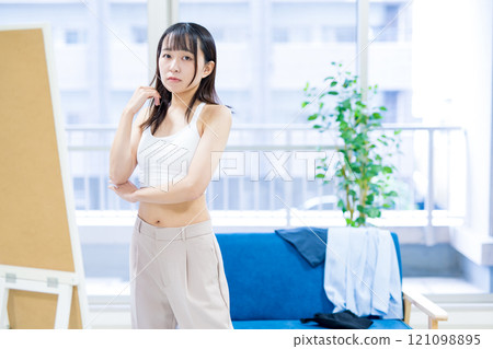 一位年輕女士在穿衣鏡前選擇運動胸罩和內衣時感到困惑。 121098895
