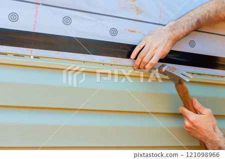 Craftsperson installing siding using hammer careful techniques on residential building in vinyl siding broad Craftsperson installing siding using hammer careful techniques on residential building in vinyl siding broad 121098966