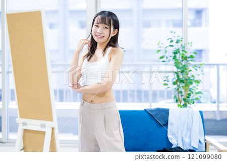 一位微笑的年輕女子在全身鏡前挑選衣服和內衣。 121099080