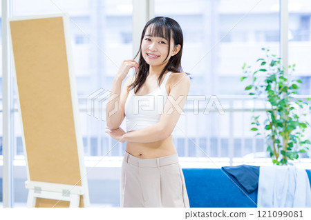 微笑的年輕女性在全身鏡前選擇衣服和內衣，選擇運動胸罩，內衣，修剪 121099081