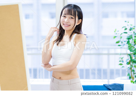 微笑的年輕女性在全身鏡前選擇衣服和內衣，選擇運動胸罩，內衣，修剪 121099082