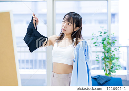 一位年輕女子在穿衣鏡前挑選運動胸罩和內衣時感到困惑。 一位年輕女子在穿衣鏡前挑選運動胸罩和內衣時感到困惑。 121099241