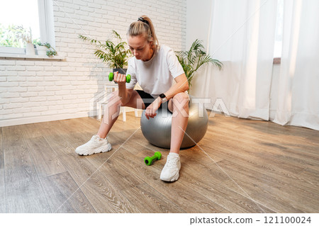 Woman exercising with dumbbells on a stability ball in a indoor space 121100024