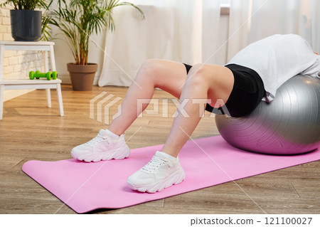 Young woman exercising on a stability ball in a bright room with plants 121100027