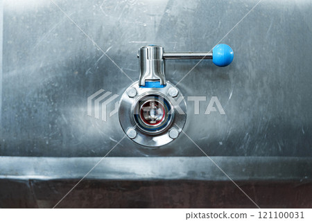 A stainless steel valve with a blue handle is attached to a large container 121100031