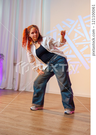 A young woman with red hair dances in a studio with a white shirt and blue jeans A young woman with red hair dances in a studio with a white shirt and blue jeans 121100061