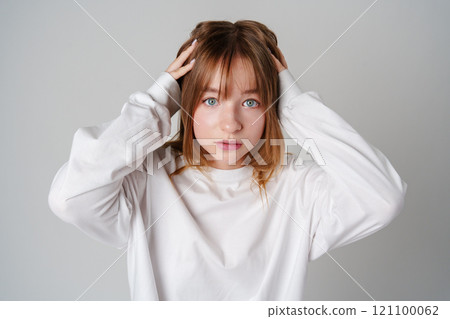 A young woman with light brown hair and blue eyes expresses surprise in a minimalist studio A young woman with light brown hair and blue eyes expresses surprise in a minimalist studio 121100062
