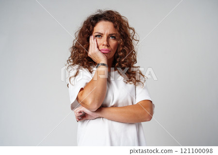Woman with curly hair thoughtfully pondering in a neutral setting Woman with curly hair thoughtfully pondering in a neutral setting 121100098