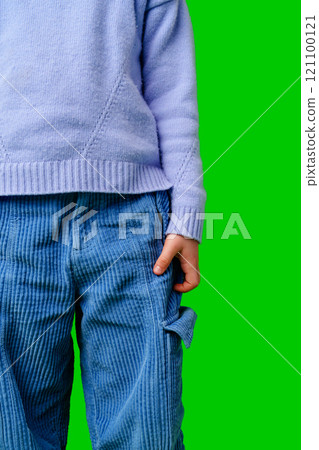 A child in a light purple sweater with blue pants stands against a vibrant green background 121100121