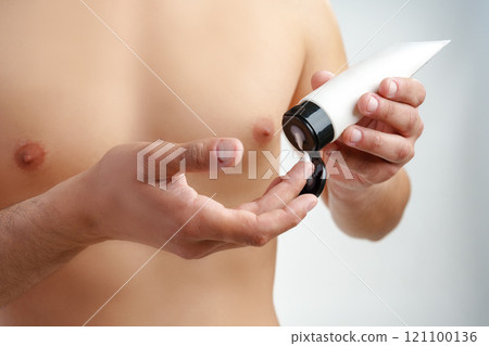 A young man applying skincare cream on his face with a focused expression, demonstrating personal grooming at home A young man applying skincare cream on his face with a focused expression, demonstrating personal grooming at home 121100136
