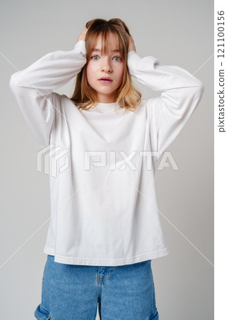 A young woman with light brown hair and blue eyes expresses surprise in a minimalist studio A young woman with light brown hair and blue eyes expresses surprise in a minimalist studio 121100156