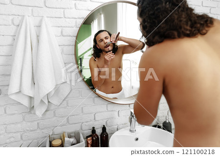 A man with curly hair grooming himself in the bathroom while looking into a round mirror 121100218