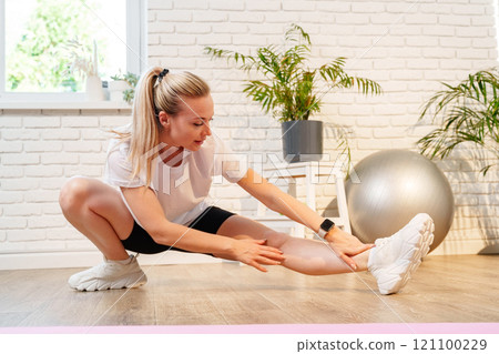 Woman performing a stretching exercise in a bright indoor Woman performing a stretching exercise in a bright indoor 121100229