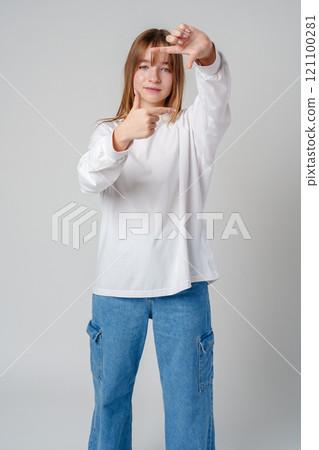 Young teen girl creating a frame with her hands while smiling indoors 121100281