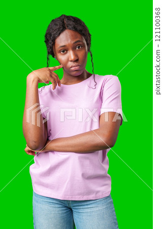 Thoughtful woman pondering in front of a bright green background during a casual moment Thoughtful woman pondering in front of a bright green background during a casual moment 121100368