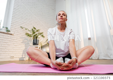 A young woman stretches on a pink mat in a bright room 121100373