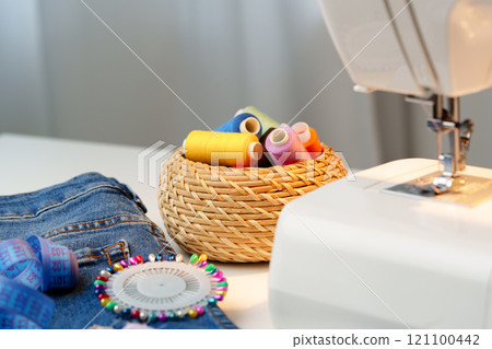 Sewing machine in use on a wooden table, stitching a light fabric in a well-lit indoor workspace 121100442