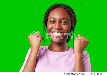 A young woman with braids expresses excitement with a clenched fist against a bright green background 121100455