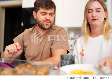 A man and a woman sit at a table in a kitchen, eating dinner A man and a woman sit at a table in a kitchen, eating dinner 121100456