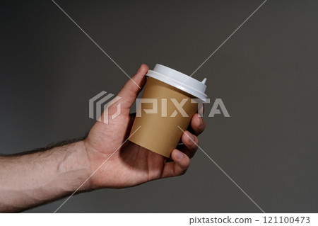 A hand holding a disposable coffee cup against a dark background A hand holding a disposable coffee cup against a dark background 121100473