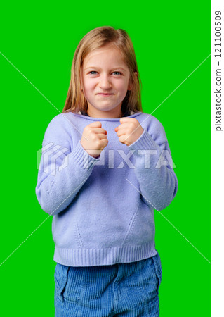 Young girl expressing determination with clenched fists against a bright green background Young girl expressing determination with clenched fists against a bright green background 121100509