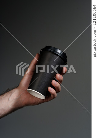 A hand holding a disposable coffee cup against a dark background A hand holding a disposable coffee cup against a dark background 121100564