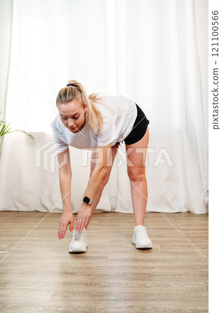 A young woman stretches during a home workout session in a bright room A young woman stretches during a home workout session in a bright room 121100566