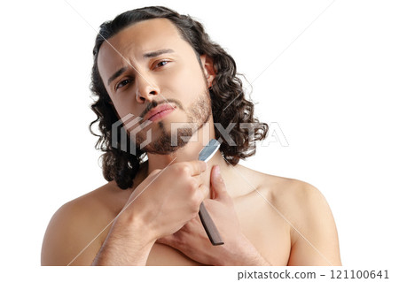 A man with curly hair grooming his beard in a well-lit space while using a straight razor 121100641