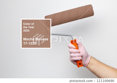 Hand holding paint roller applying mocha mousse color on wall indicating color of the year for 2025 Hand holding paint roller applying mocha mousse color on wall indicating color of the year for 2025 121100690