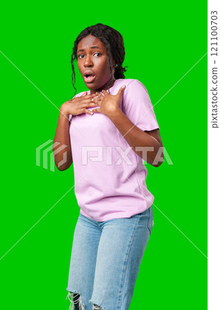 Surprised young woman against a vibrant green background expressing astonishment or shock 121100703