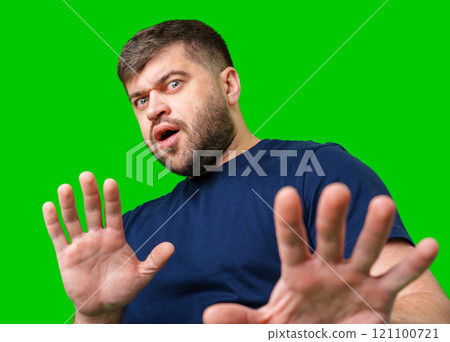 A man with a serious expression holds up both hands in a stopping gesture against a bright green background 121100721