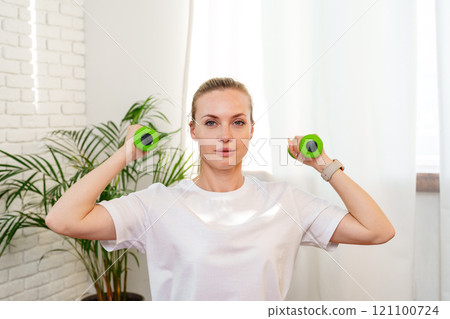 A woman exercises with green dumbbells at home in a bright room A woman exercises with green dumbbells at home in a bright room 121100724