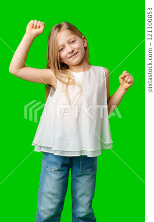 Young girl joyfully dancing with raised arms against a green background 121100853