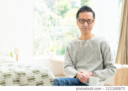 Middle-aged man drinking coffee in bedroom 121100873